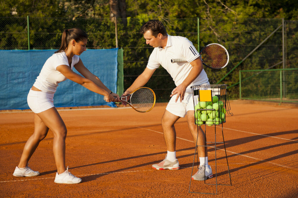 Front view of tennis coach teaching young woman the position of racket at backhand